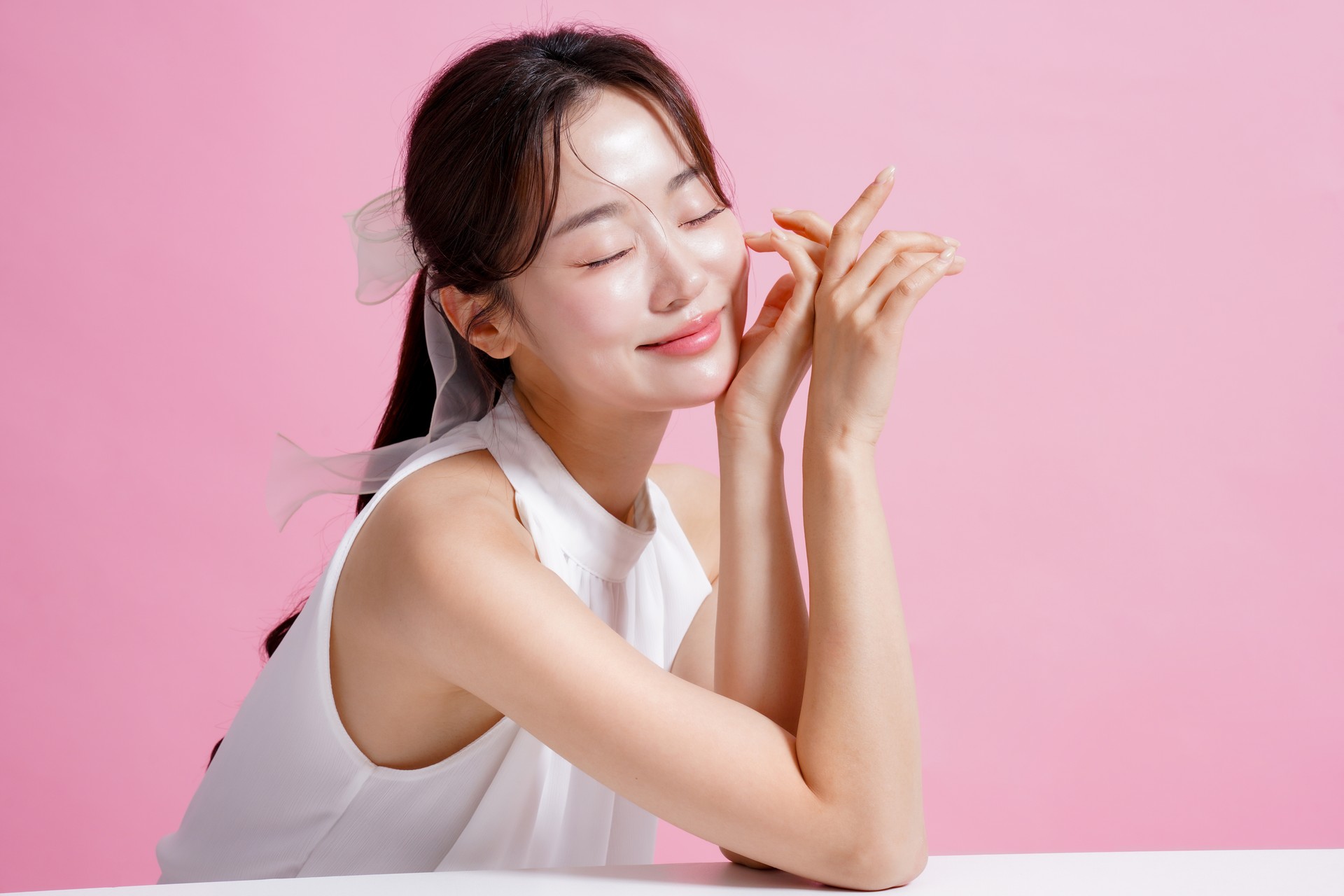 Light portrait of a young Asian woman shot against a pink background