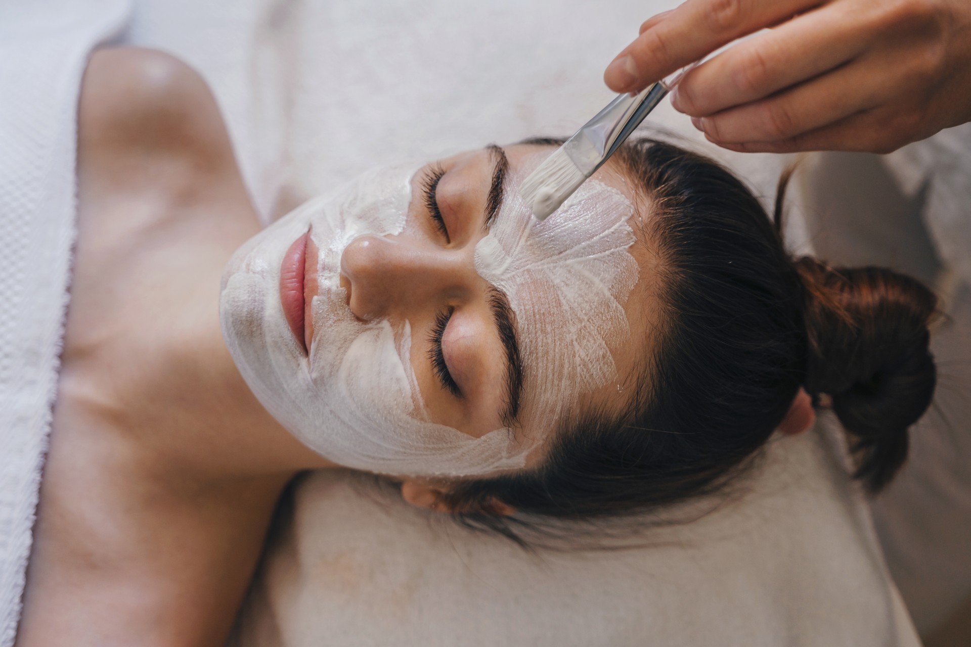 Woman getting facial nourishing mask by beautician at spa salon. Skincare spa relax concept.